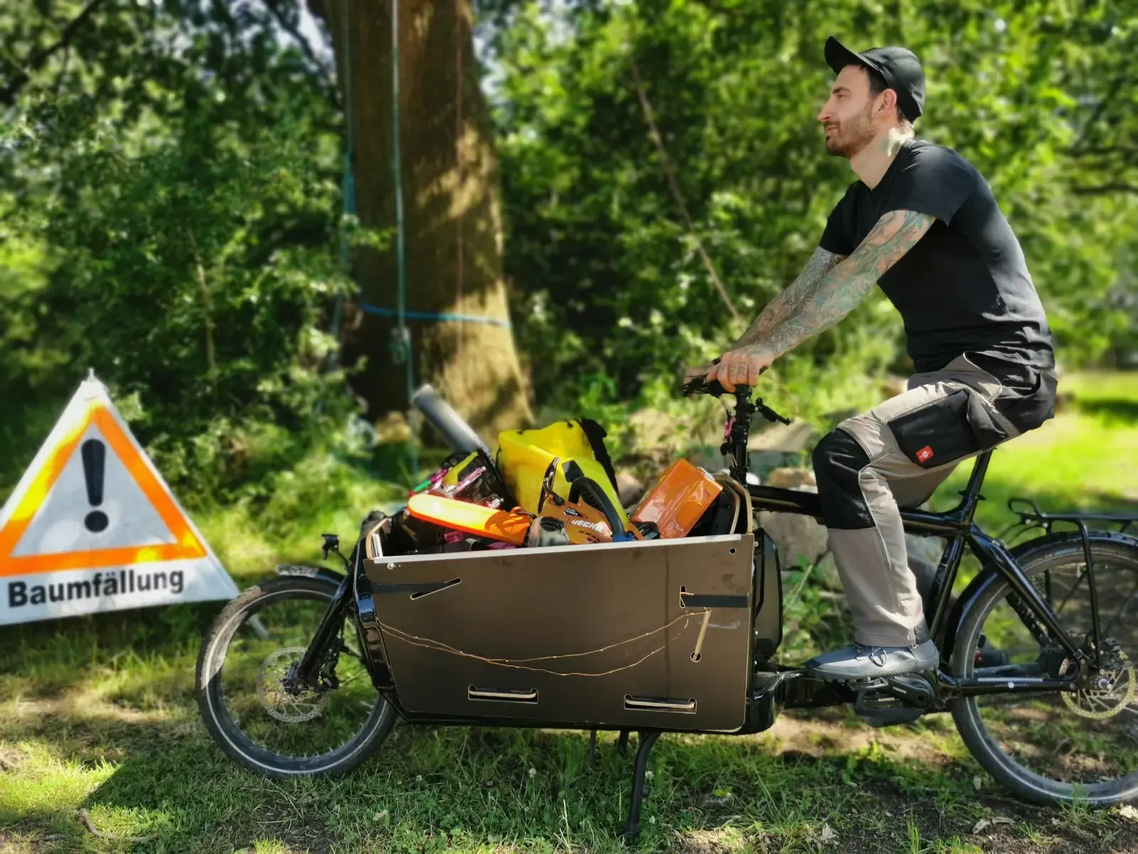Lastenrad voll mit Kletterausrüstung und Motorsäge, daneben das Warnschild Baumfällung